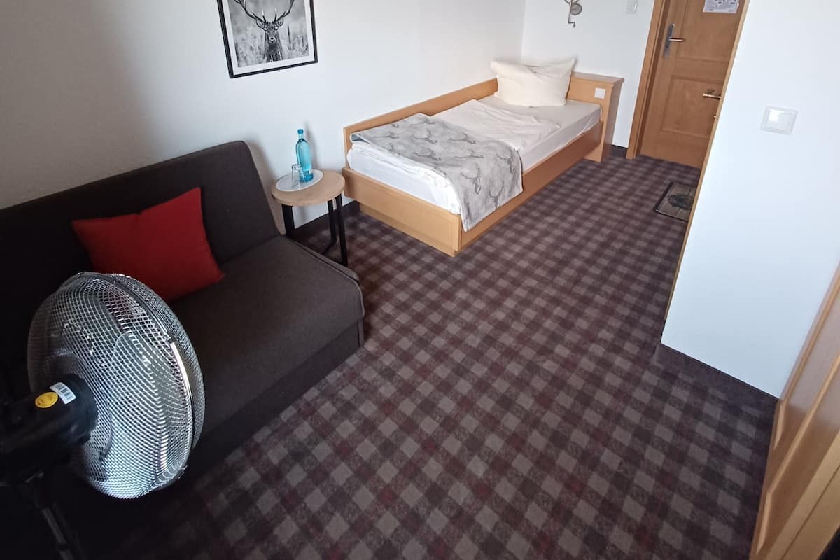 Une chambre d’hôtel avec un lit, un canapé, une petite table, une lampe, un tableau au mur et un sol à carreaux.