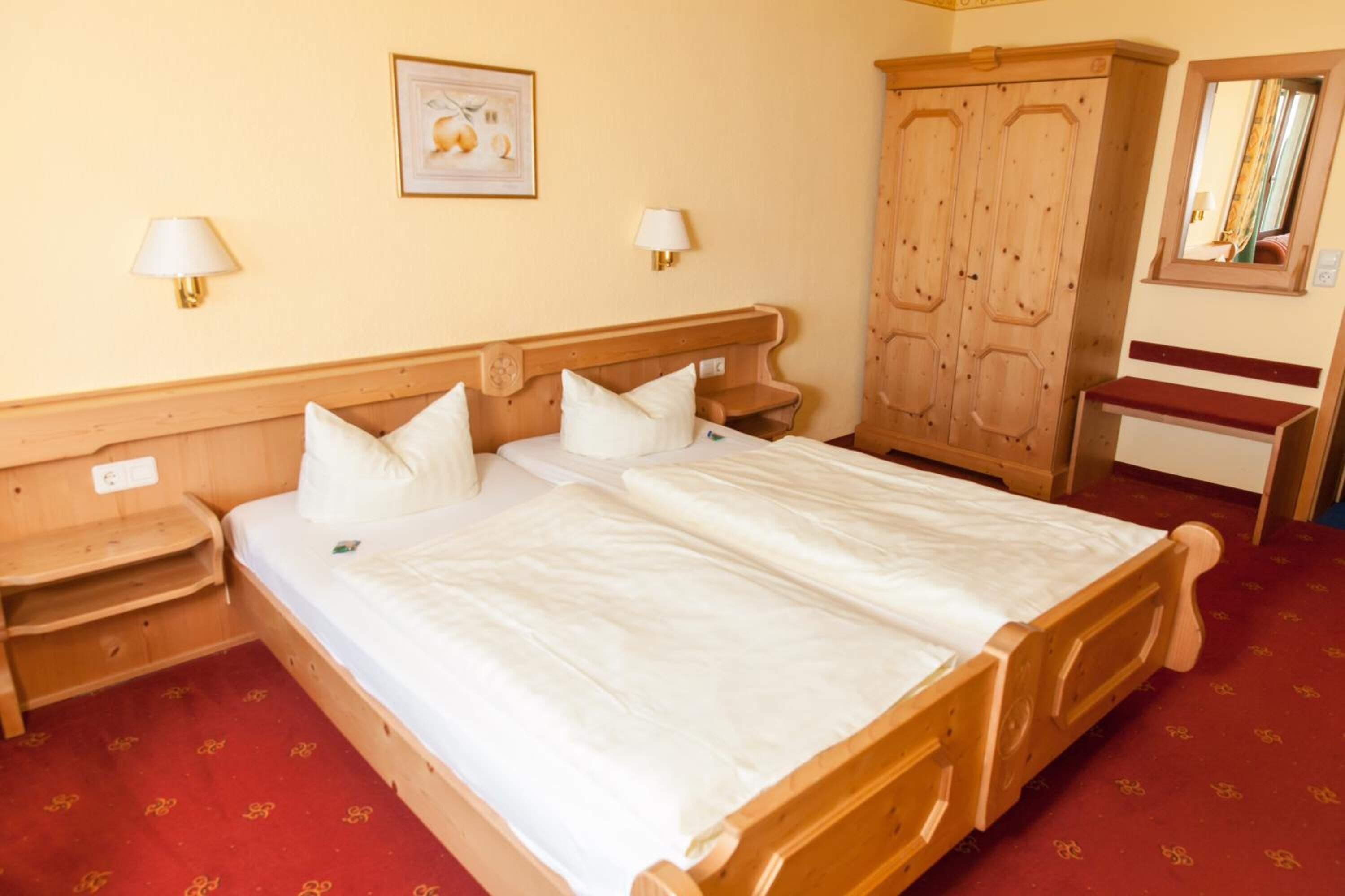 A double bed with white linens, wooden headboard, bedside tables, and a red carpeted floor.
