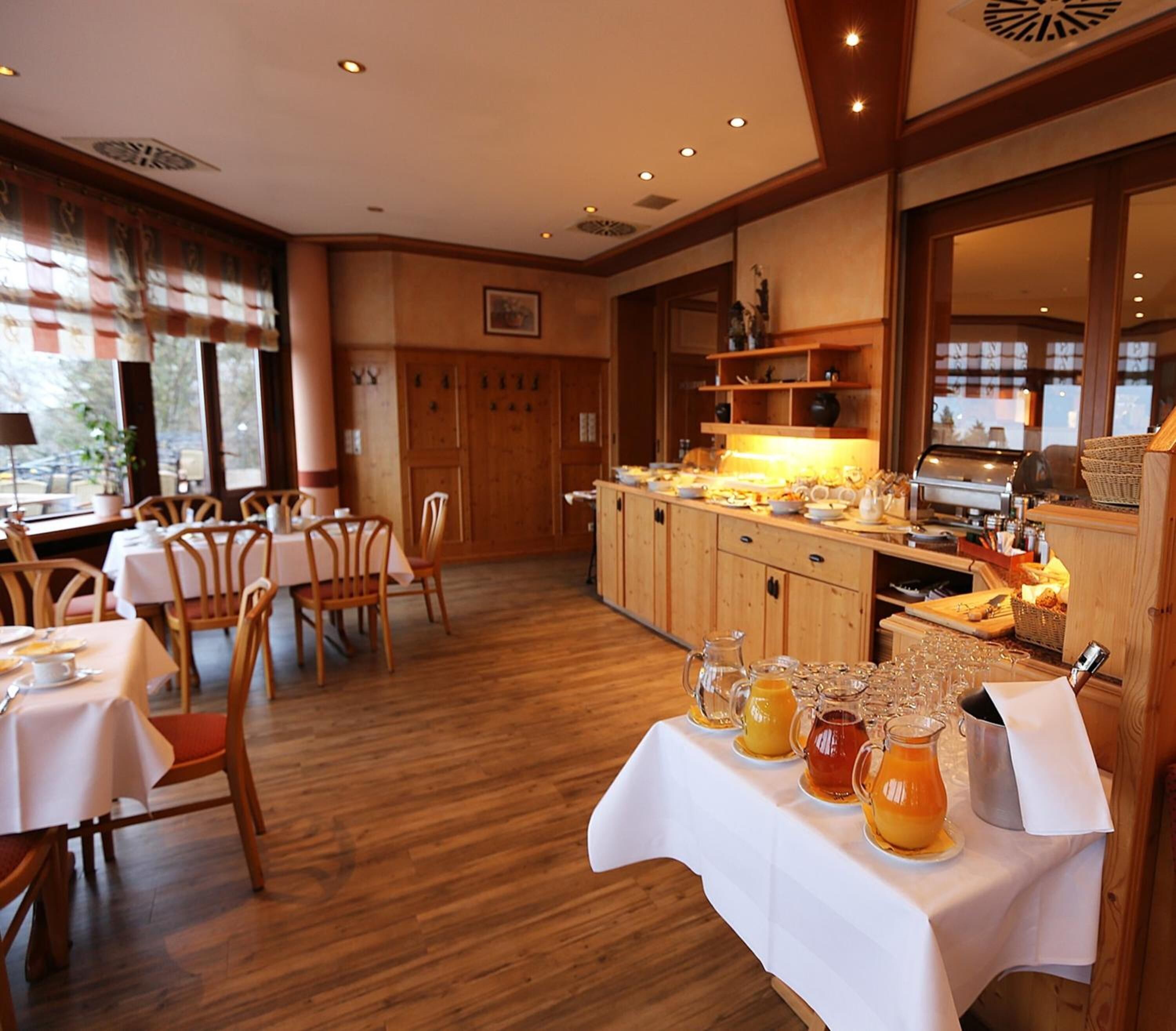 Un comedor con mesas y sillas de madera, una barra de buffet con diferentes opciones de comida y una cocina visible al fondo.