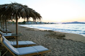Una playa con sillas de descanso y una sombrilla de paja.