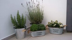 Trois pots à fleurs en métal, contenant des plantes, sont posés sur un sol carrelé devant un mur blanc.