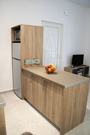 A kitchen with wooden cabinets, a microwave, a fruit bowl, and a television. - Orama II (Chania)