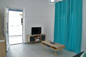 A room with a television on a wooden cabinet, a small table with a blue bowl, and a teal curtain. - Orama II (Chania)