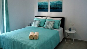 Un lit bien fait, avec une literie de couleur turquoise et deux oreillers, une petite table de chevet avec une lampe, et deux tableaux accrochés au mur.