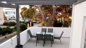 Un balcon avec une table et des chaises, un pot de fleurs et une vue sur la rue et les arbres.