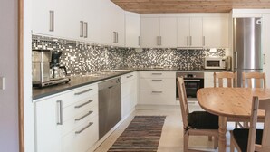 A modern kitchen with white cabinets, a black and white tiled backsplash, stainless steel appliances, and a wooden dining table with chairs.