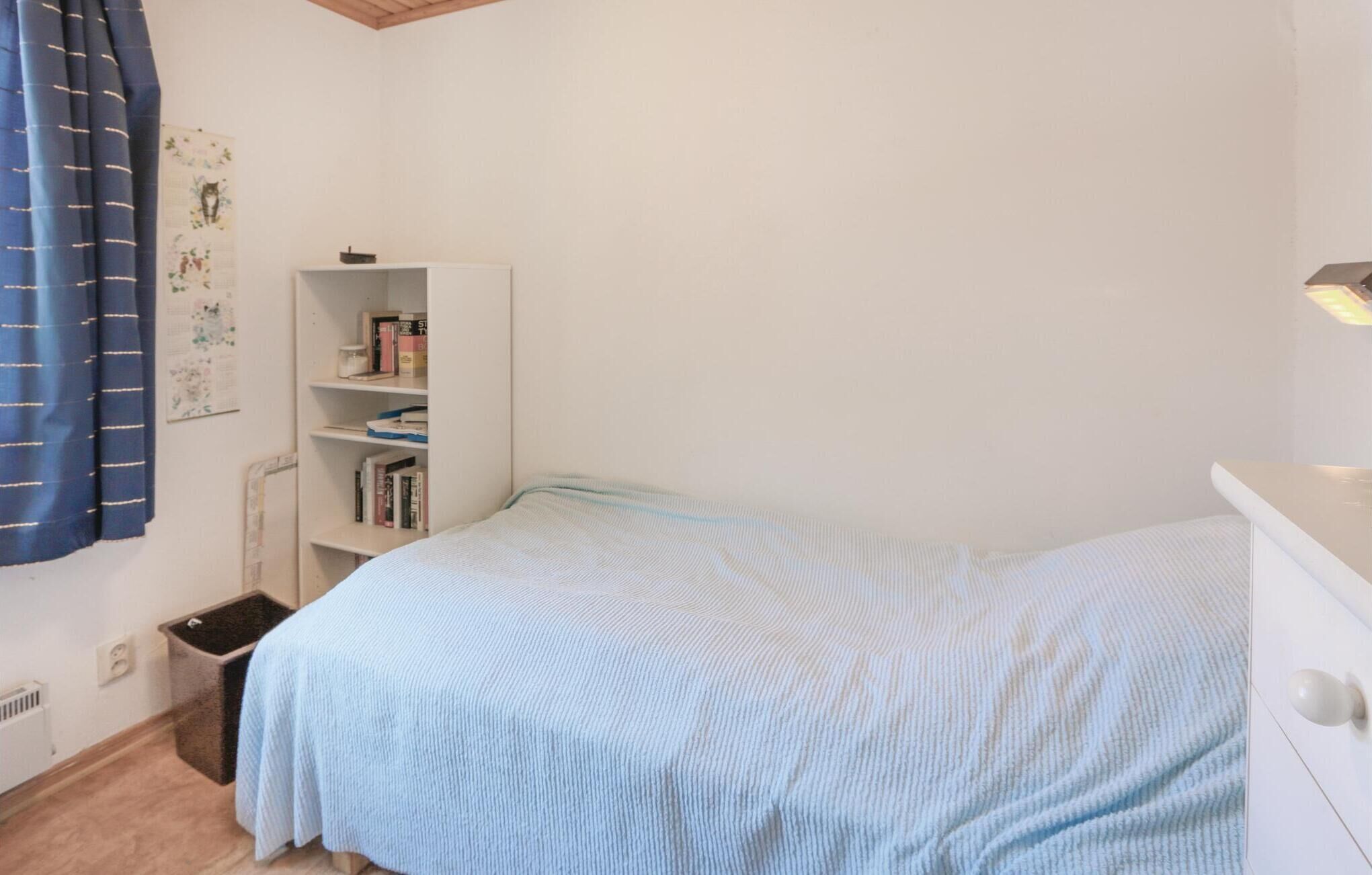 Une petite chambre à coucher avec un lit simple, une armoire blanche, une bibliothèque et un radiateur.