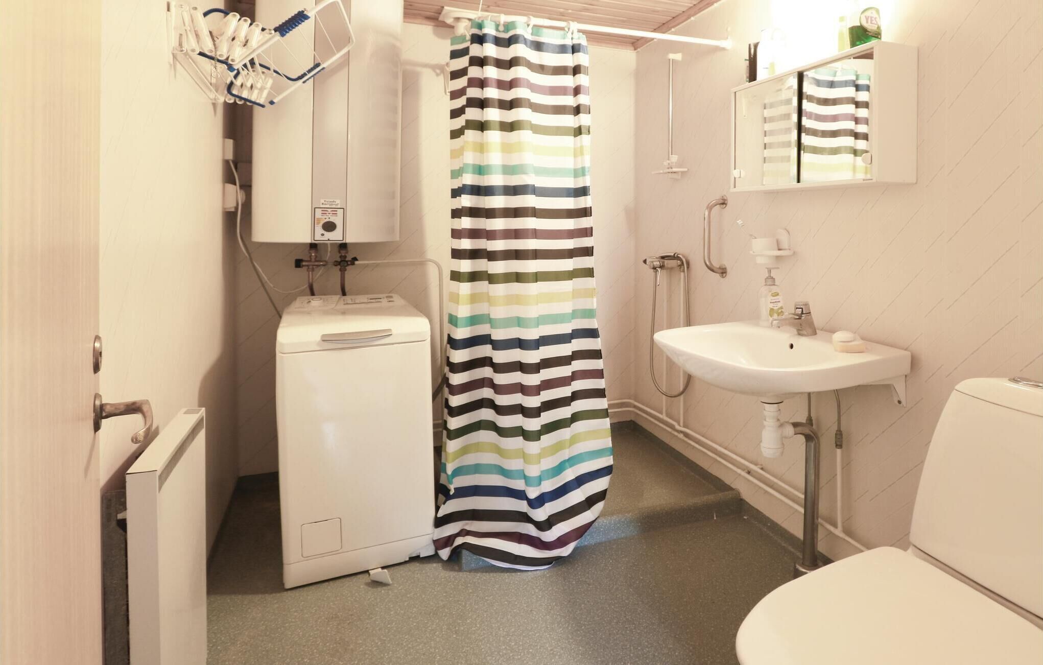 A compact bathroom with a washing machine, a striped shower curtain, a sink, and a toilet.