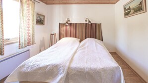 A double bed with a white quilt, a wooden headboard, two wall-mounted lamps, and a window with curtains.