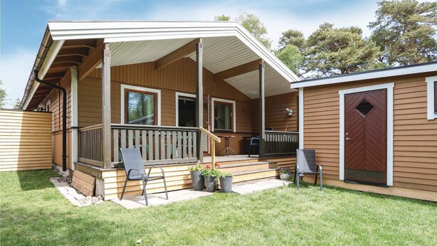 A wooden house with a porch, two chairs, and a small garden area.