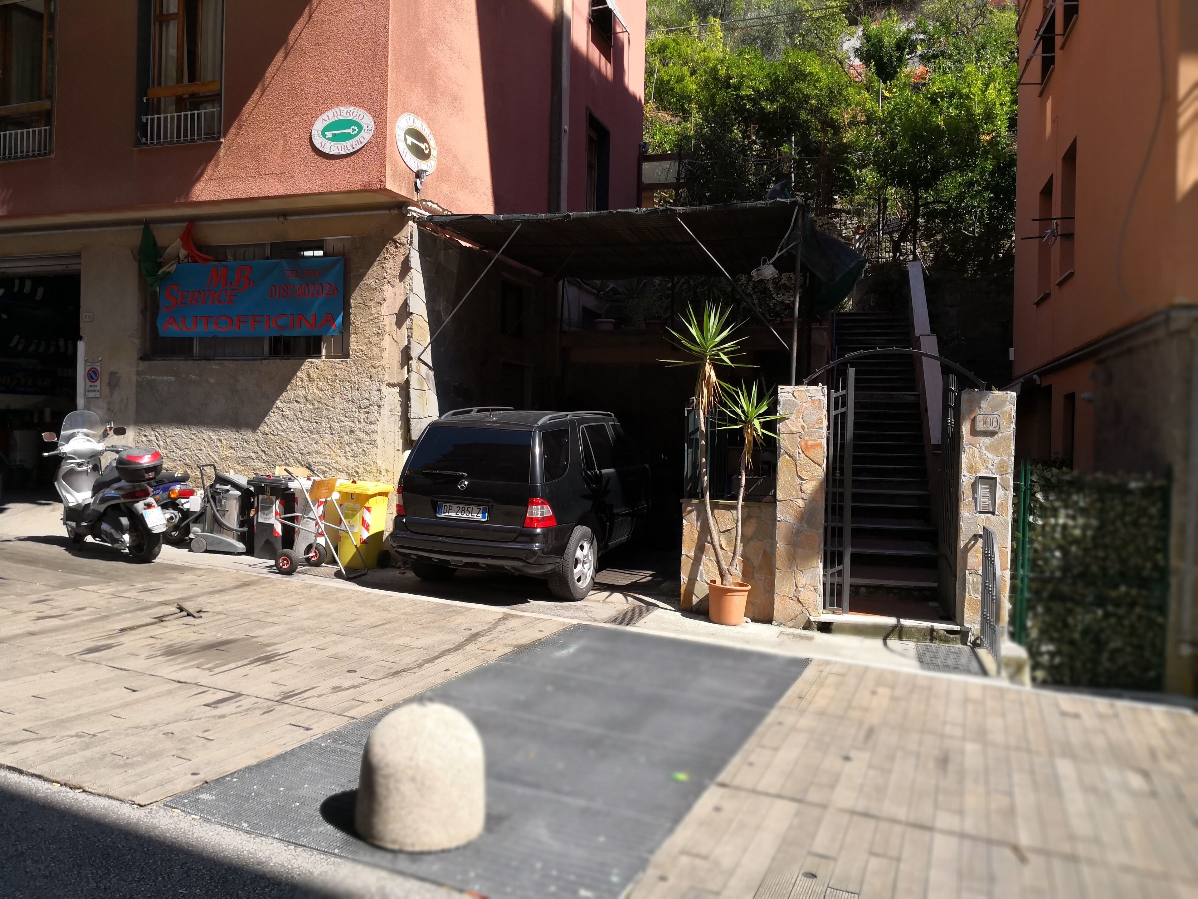 A parking area with a black SUV, a motorcycle, and a yellow trash bin.
