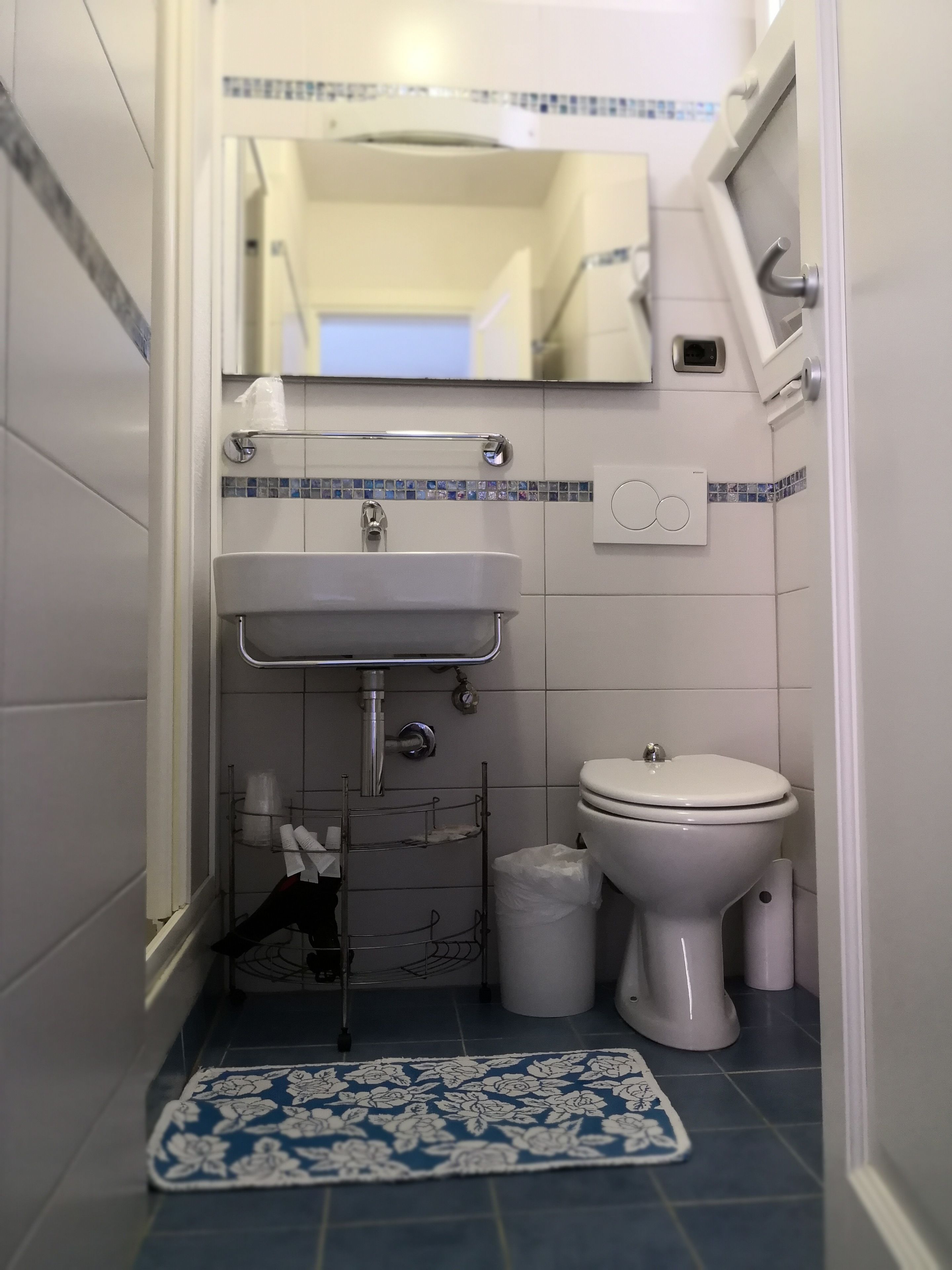 Une petite salle de bain avec un lavabo blanc, des toilettes et un tapis à motifs bleus et blancs sur le sol.