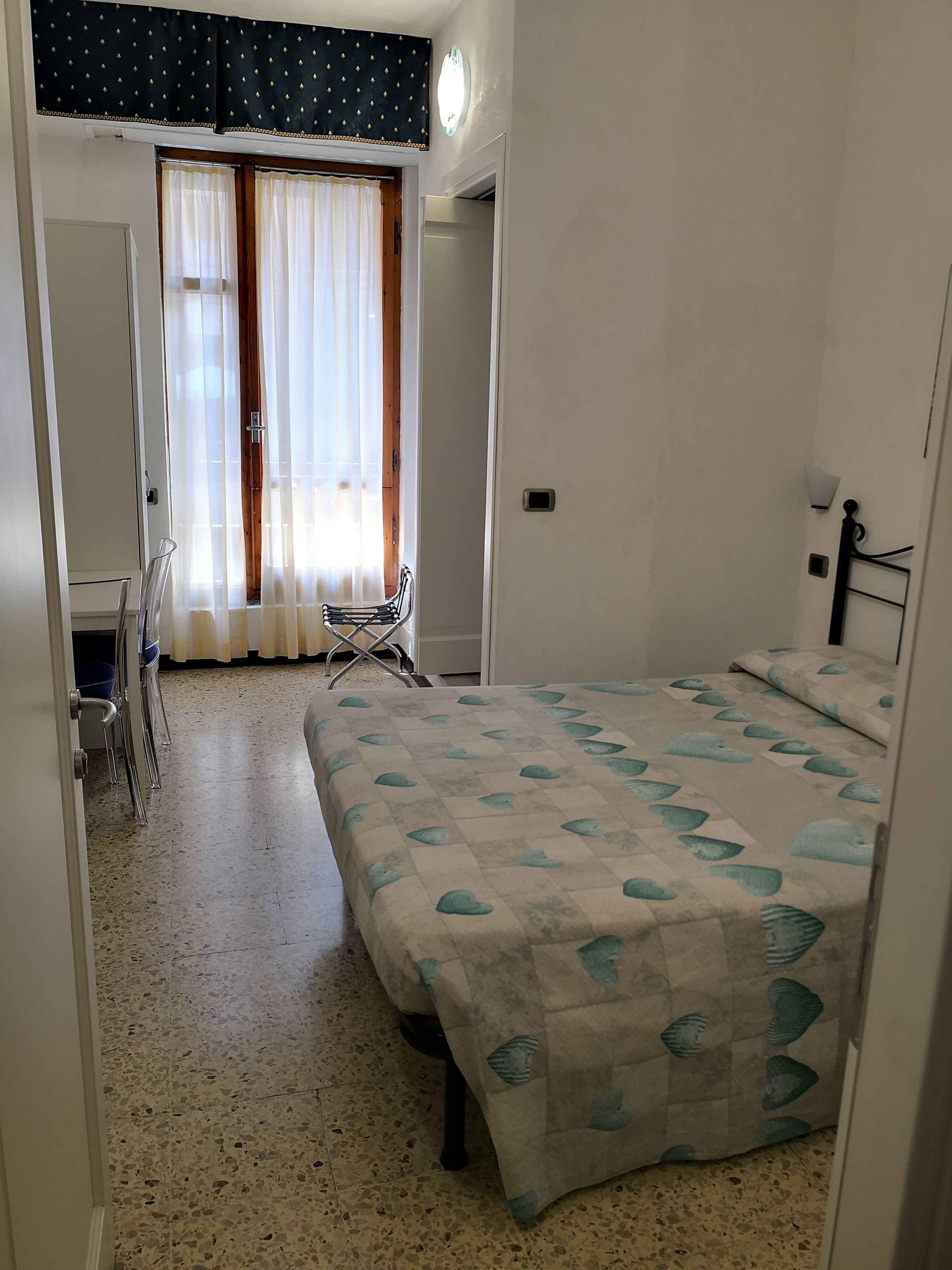 A bedroom with a bed, a chair, a desk, and a window with curtains.
