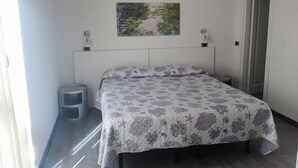 A bedroom with a bed, a small stool, a painting on the wall, and a door. - Albergo Al Carugio (Monterosso al Mare)