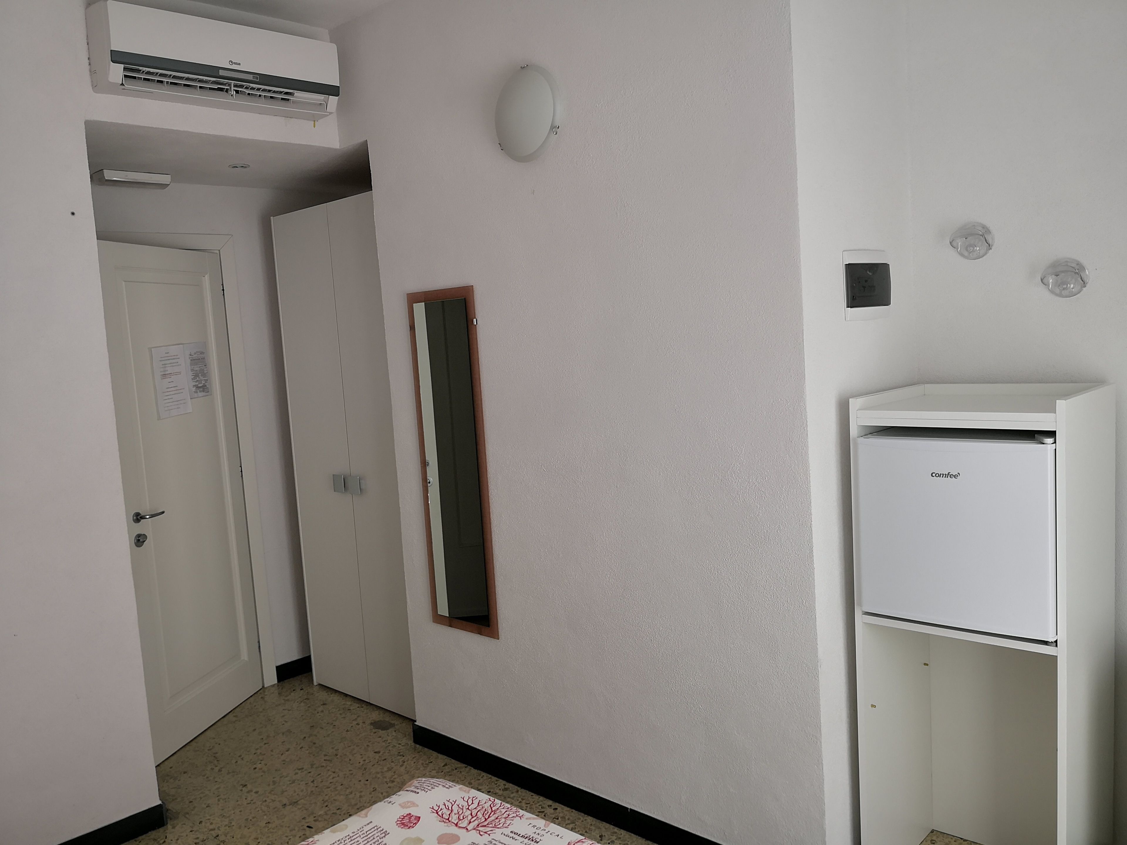 A hallway with a white door, a small mirror, and a white refrigerator.