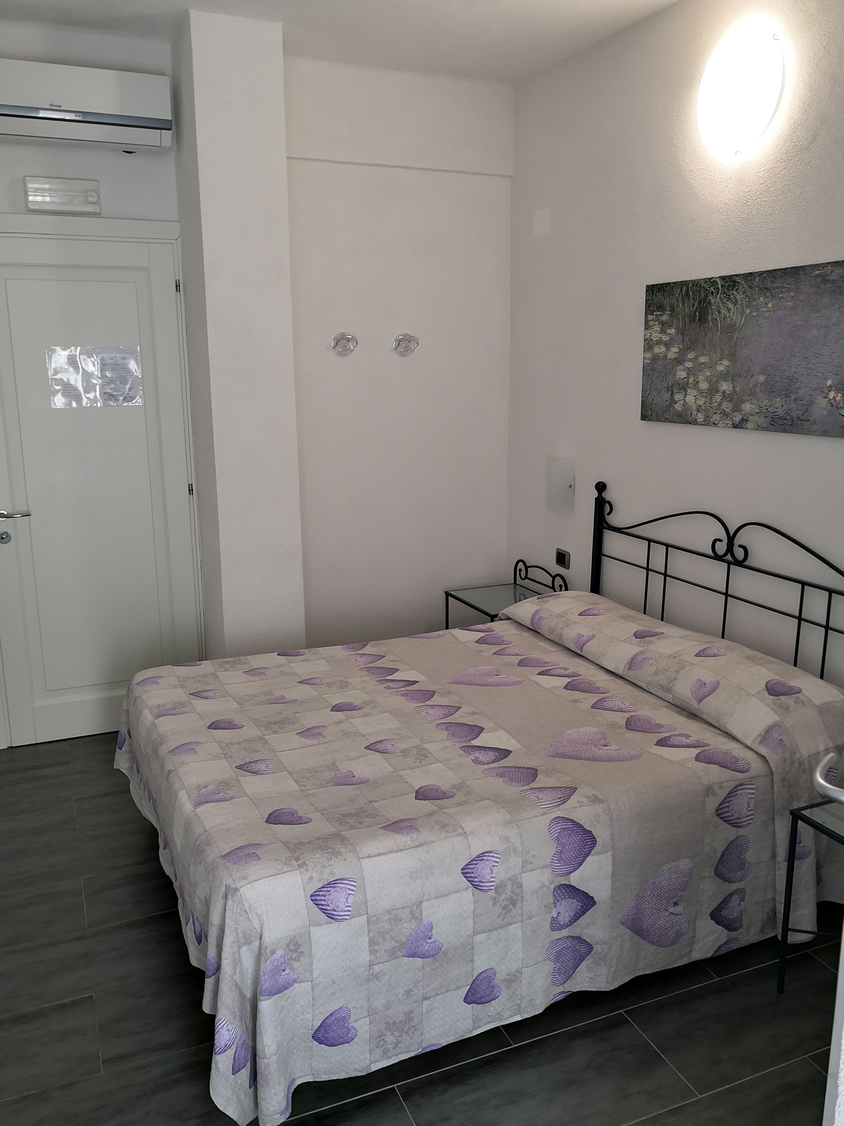 Un dormitorio con cama, mesita de noche, luz de pared y puerta.