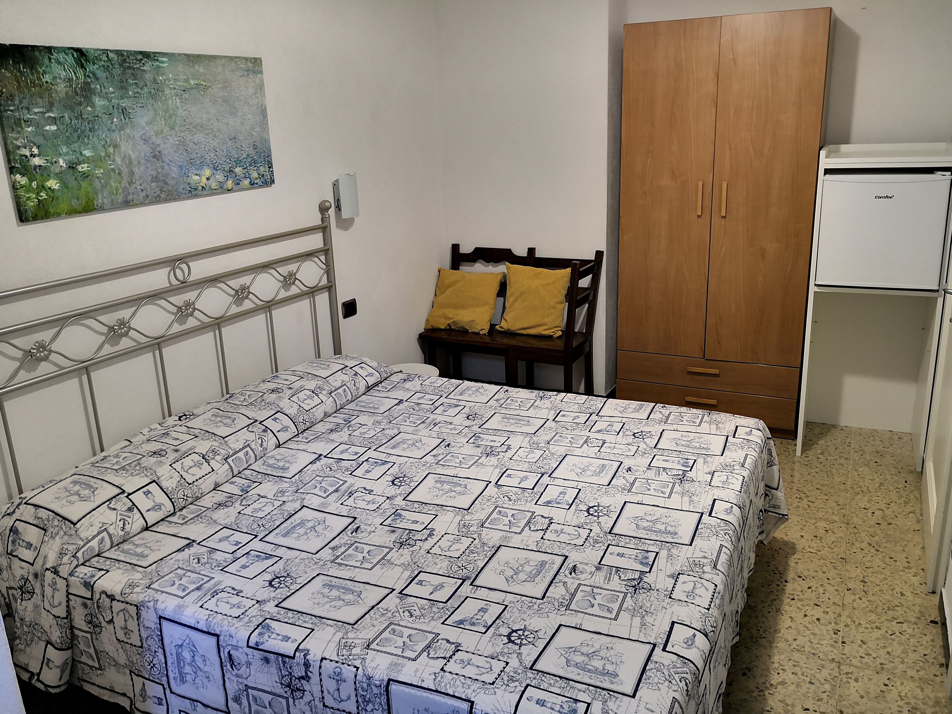 Une chambre à coucher avec un lit, une armoire en bois, une petite table avec une chaise et un tableau accroché au mur.