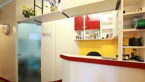 A reception area with a glass door, a red and white counter, and shelves with various items. - Albergo Al Carugio (Monterosso al Mare)