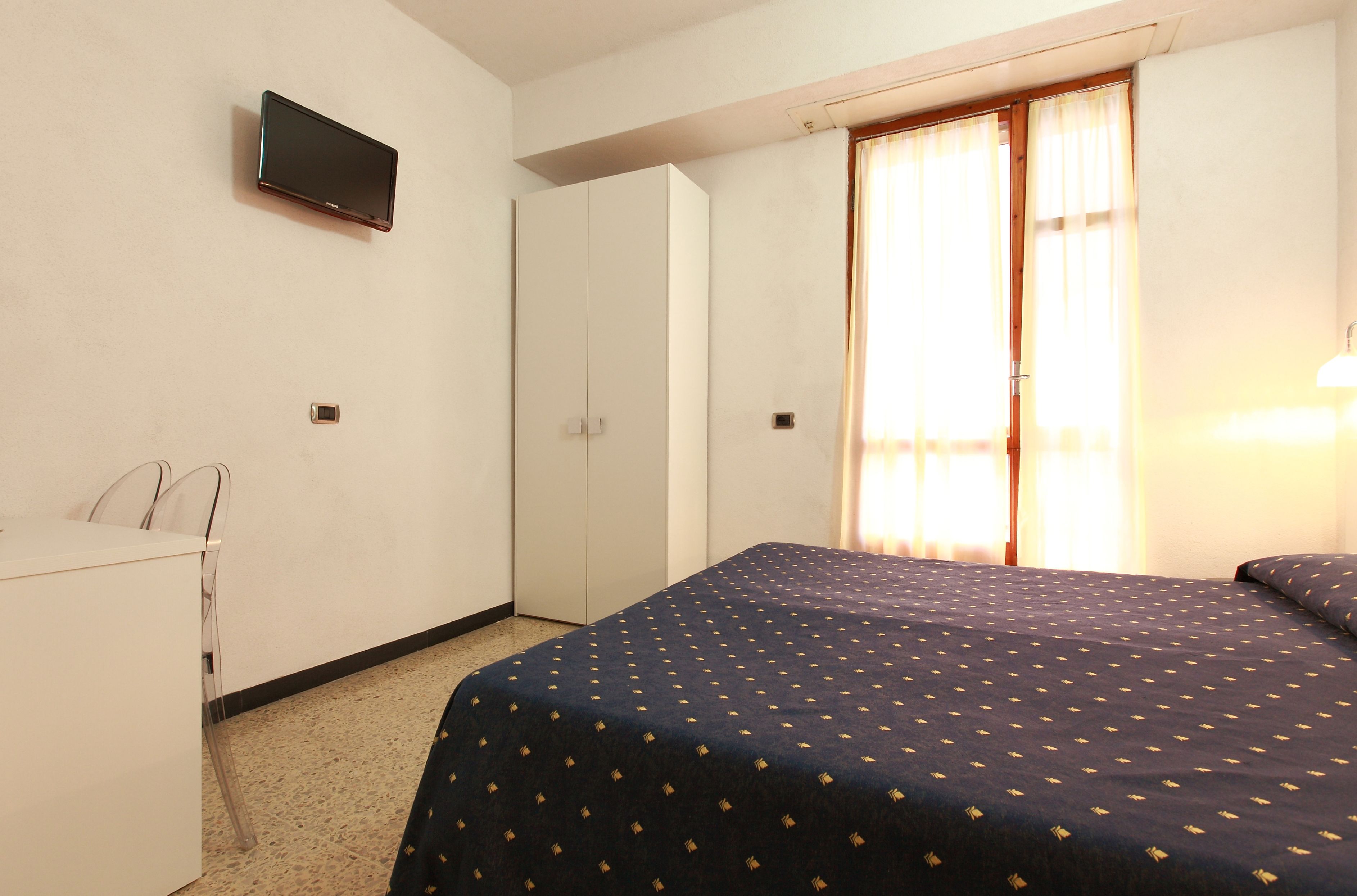 A hotel room with a bed, a desk, a wardrobe, and a television on the wall.