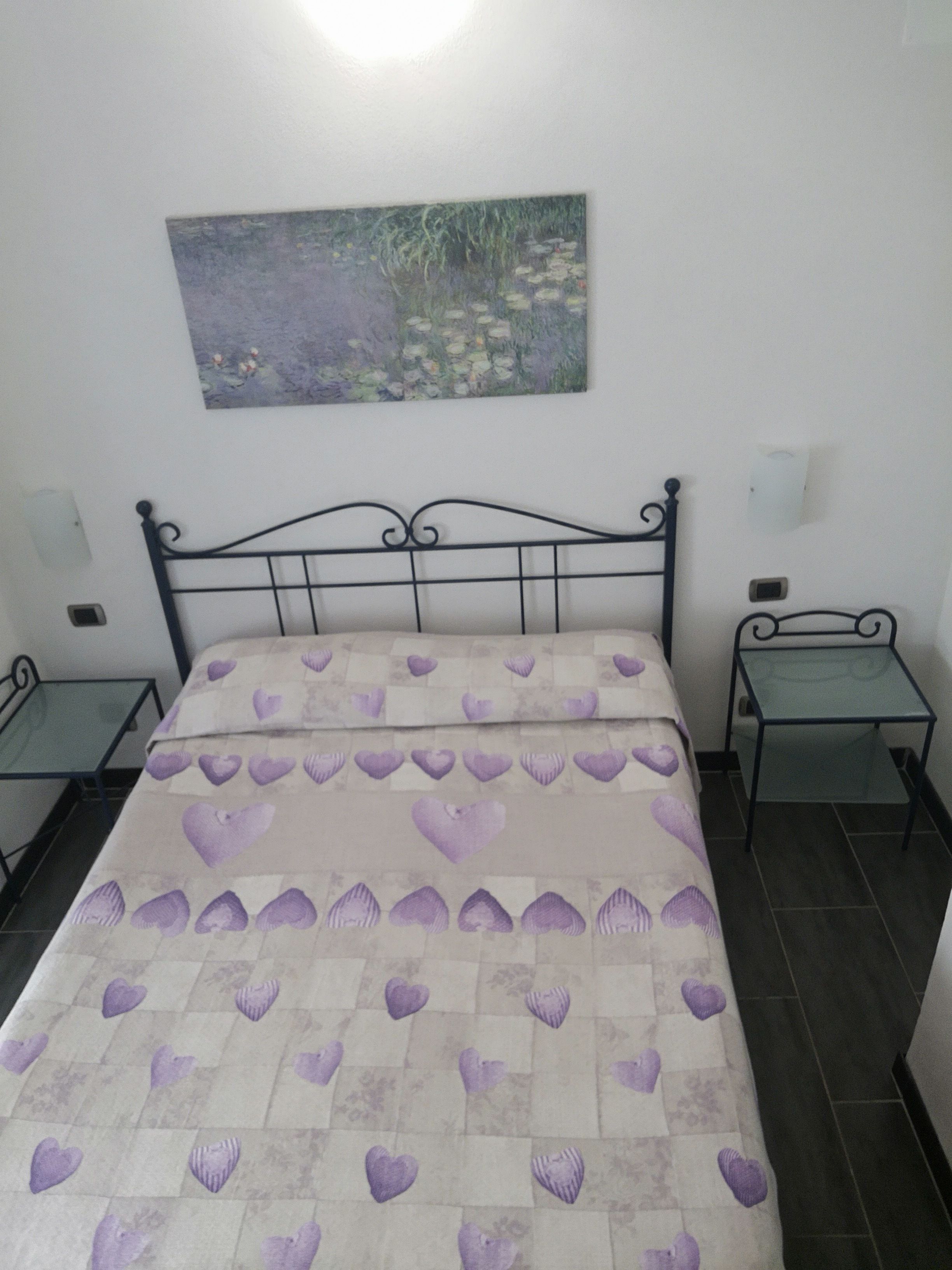 Een bed met een beddegoed met patroon, een schilderij aan de muur en twee nachtkastjes met lampen.