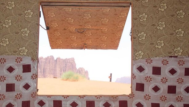 A window with a patterned curtain, a view of a desert landscape, and patterned walls. - Wadi Rum Protected Area Camp (Wadi Rum)