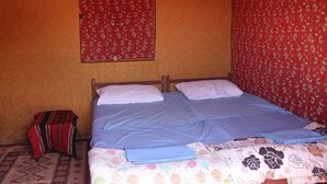 A single bed with a blue bedspread and pillows, a red floral curtain, and a patterned rug. - Wadi Rum Protected Area Camp (Wadi Rum)