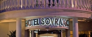 Exterior del Hotel Sovrano, con un letrero llamativo y un elemento arquitectónico circular sobre la entrada.