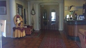 A hotel lobby with a long red carpet, a statue, and a reception desk. - Hotel Sovrano (Alberobello)