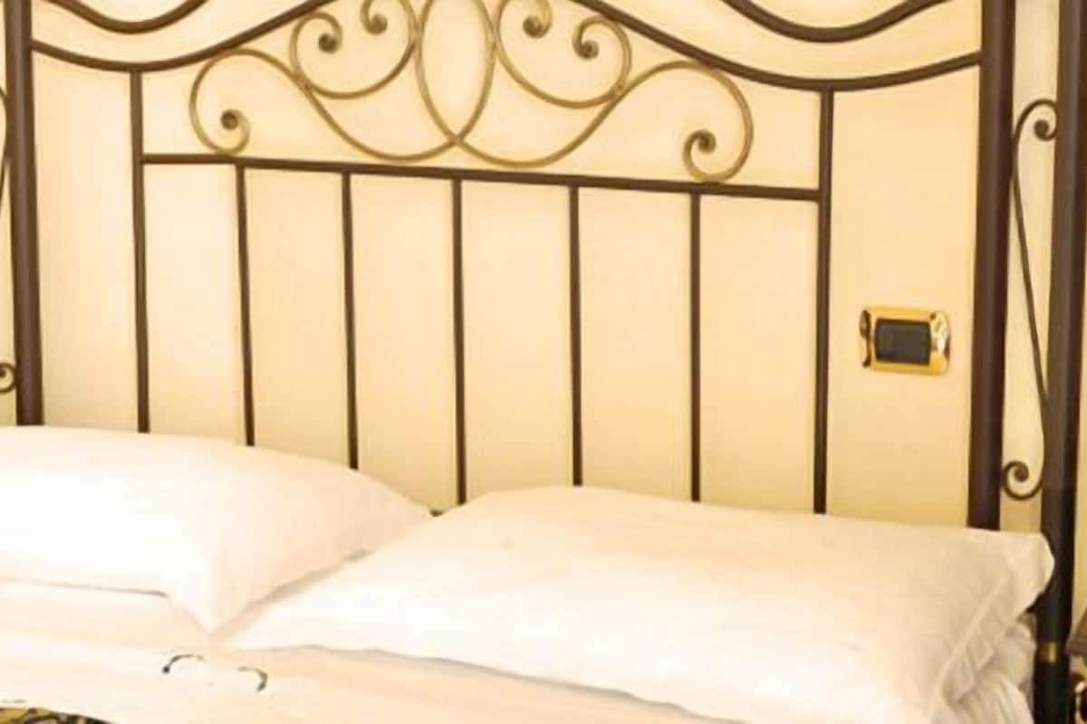 Un letto con una testiera in metallo, un comodino con una lampada e un tavolino con un vaso di fiori.