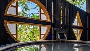 Una piscina con estructura de madera y un banco de piedra, rodeada de paredes de madera oscura con grandes ventanas circulares.