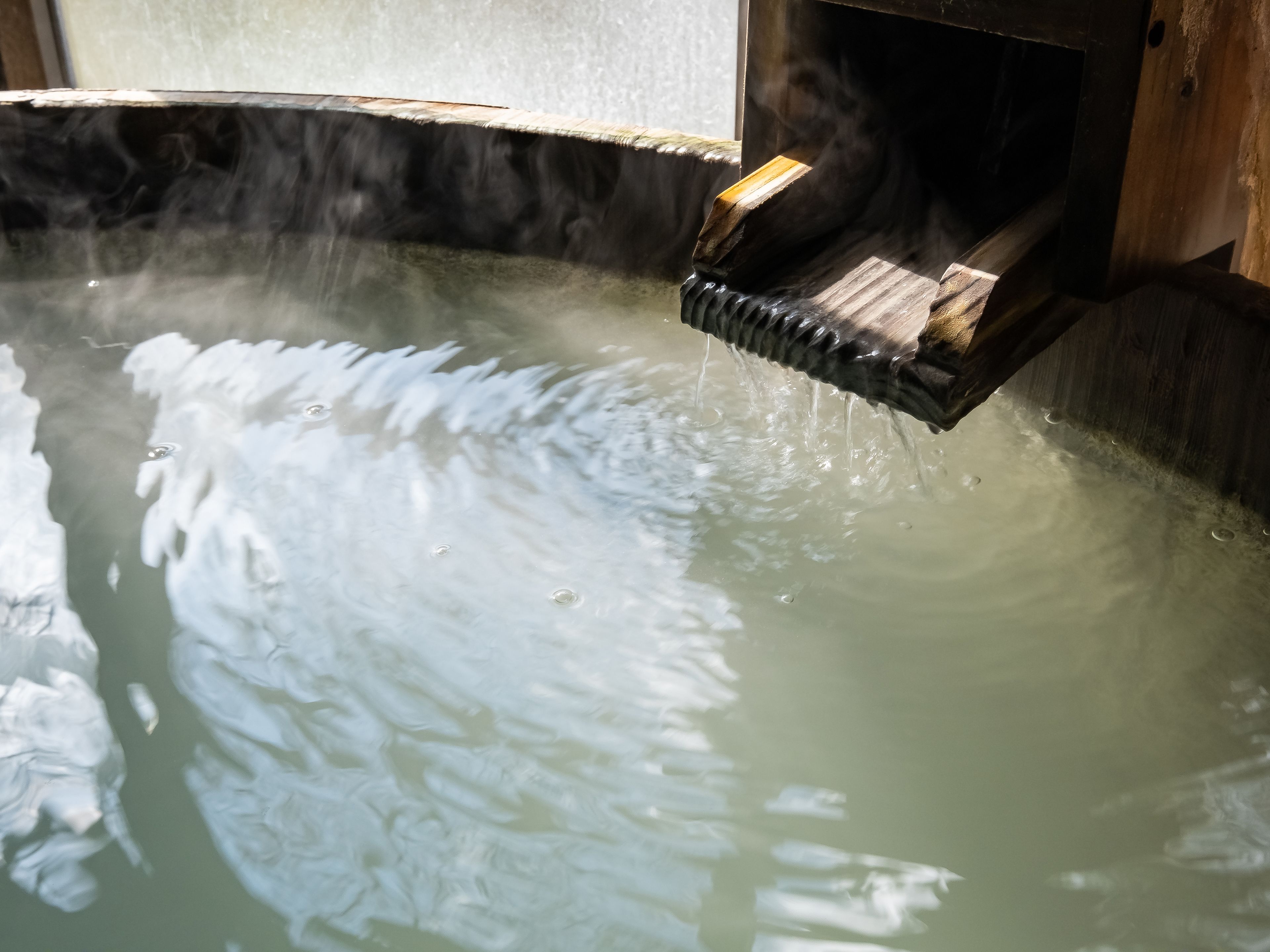 A hot spring with wooden steps leading into the water, surrounded by stone walls.