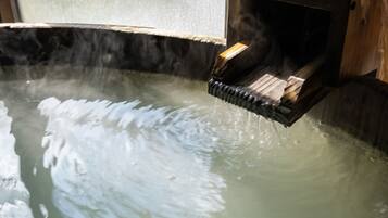 A hot spring with wooden steps leading into the water, surrounded by stone walls.