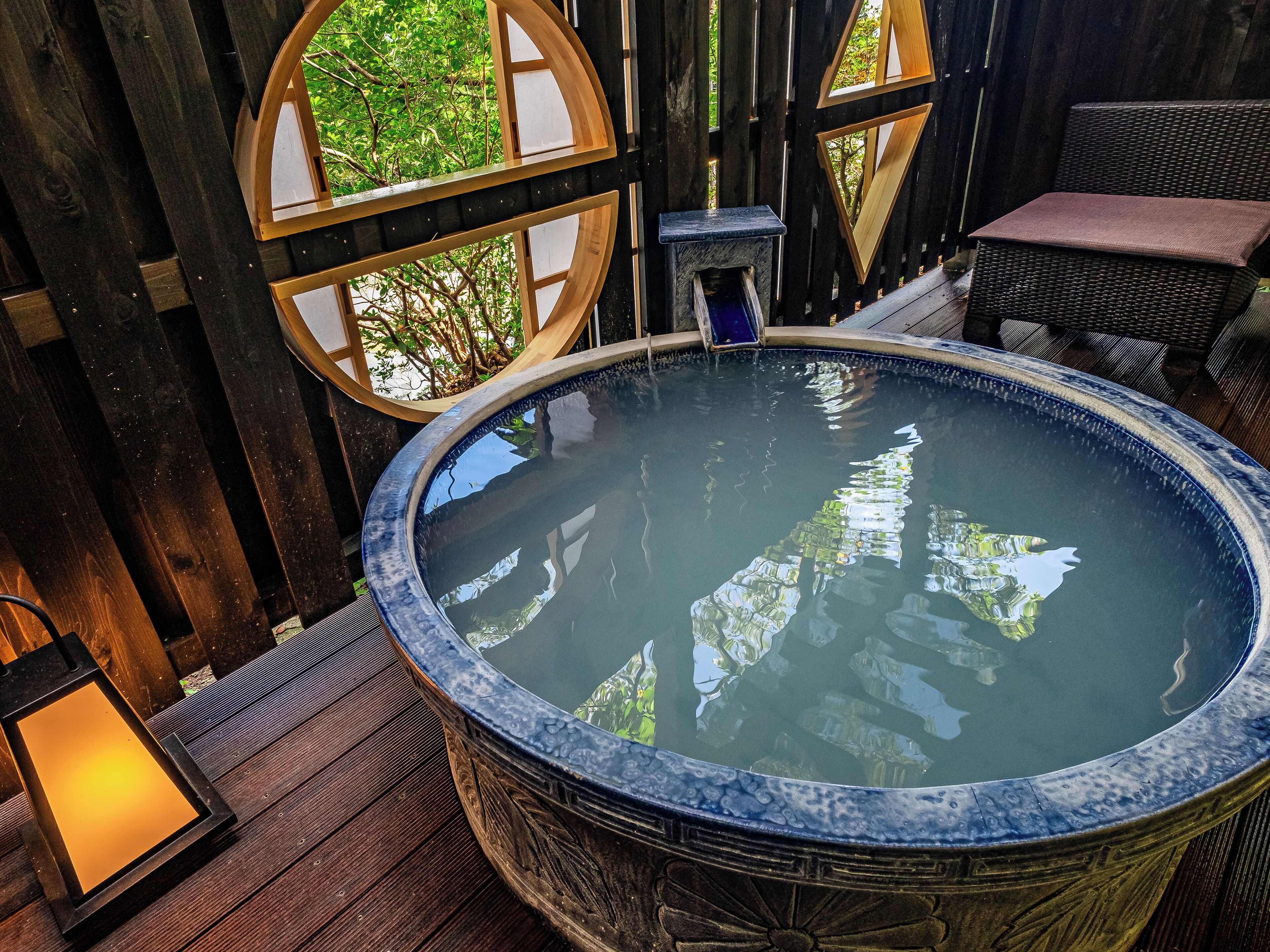 A hot tub with a wooden deck, a wooden fence, and a view of greenery.