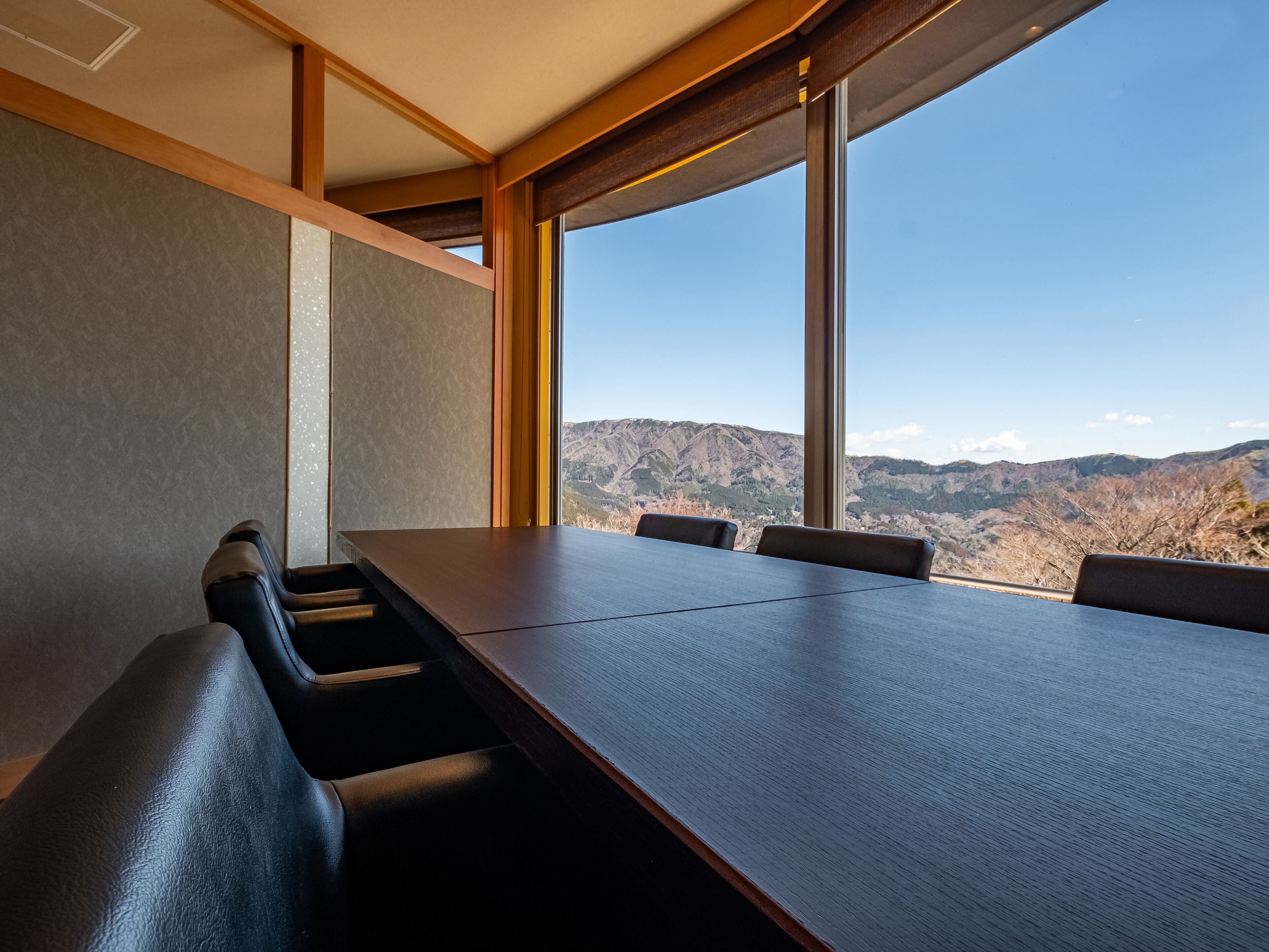 A conference room with a long table and chairs, large windows with a mountain view.