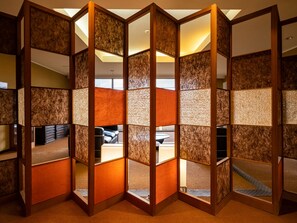 Una habitación con un separador tradicional japonés tipo shoji, un sofá de cuero negro y una pequeña mesa redonda.