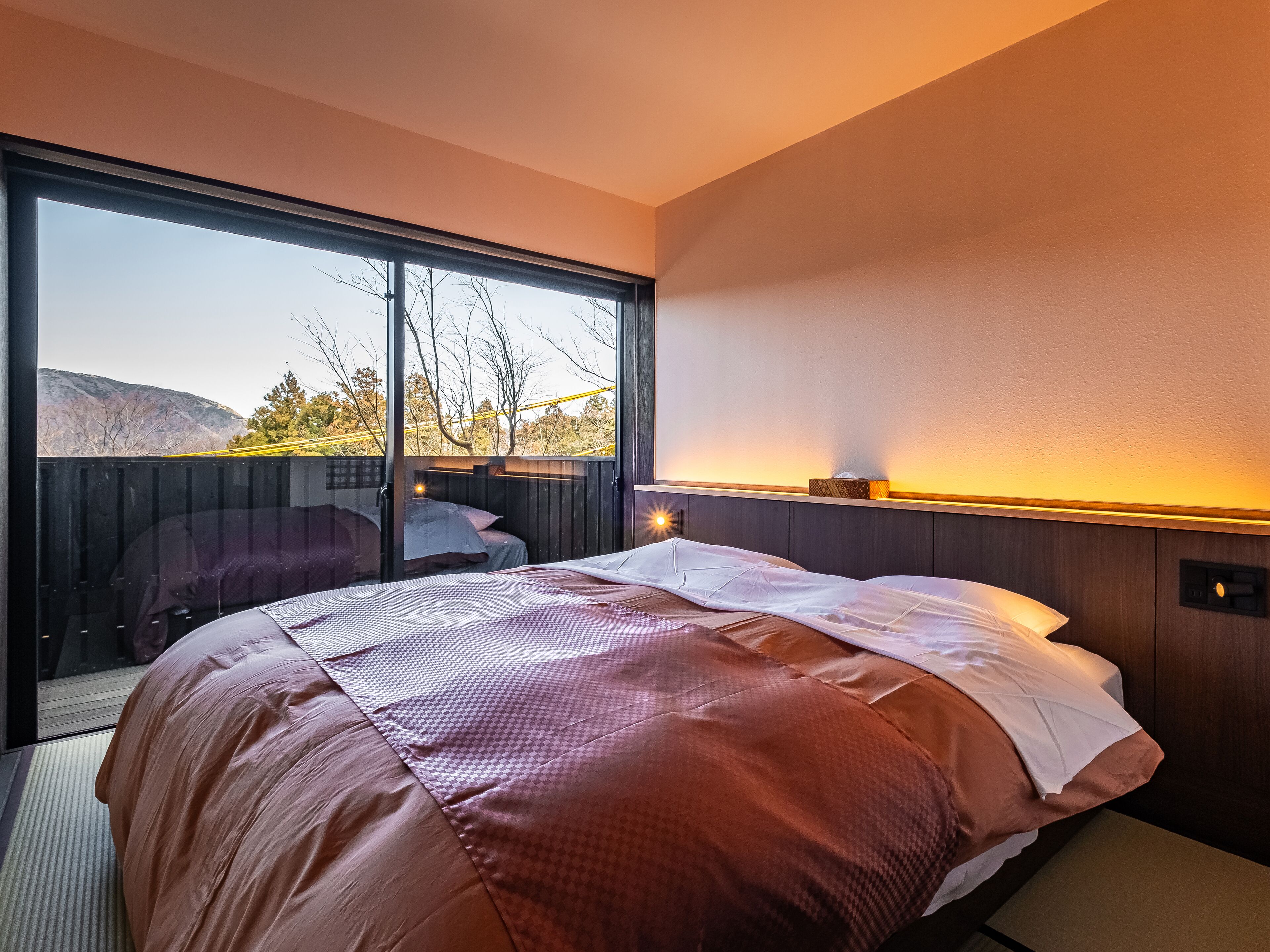 A bedroom with a large bed, a sliding glass door leading to an outdoor area, and a nightstand with a lamp.