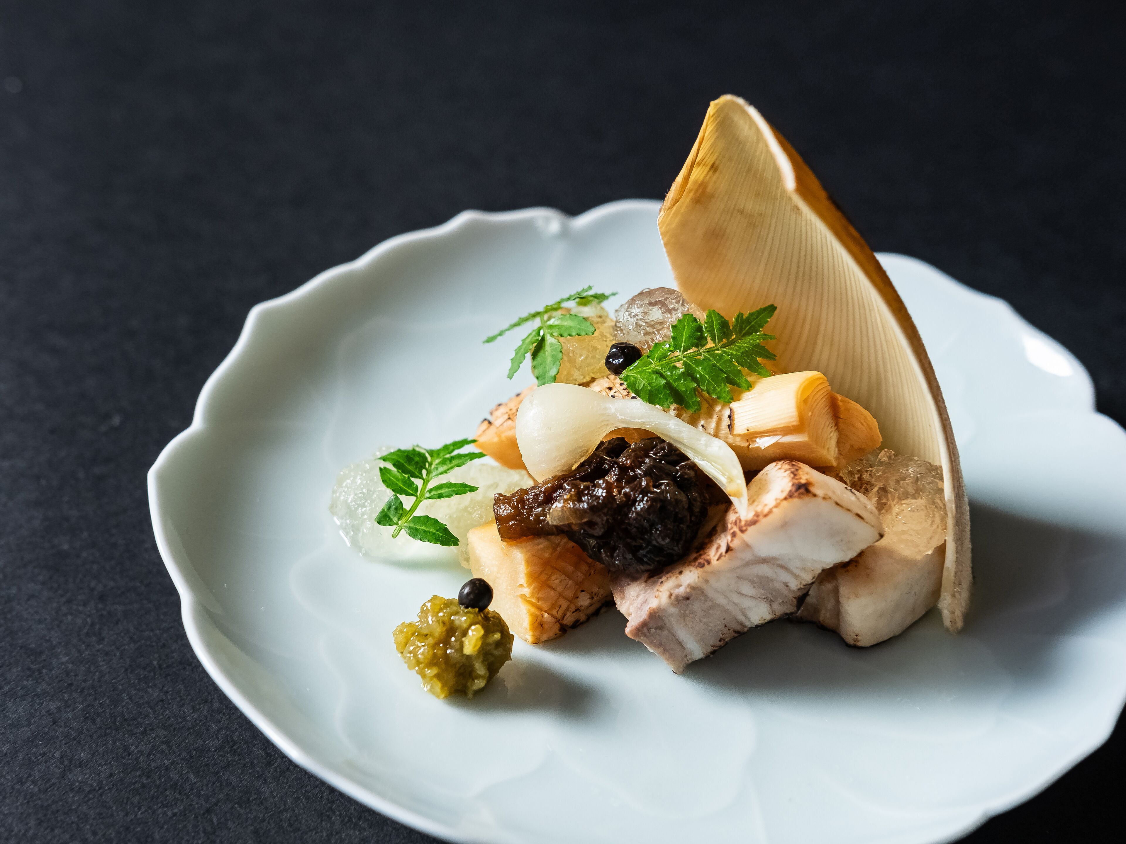 A white plate with a variety of food items including a piece of meat, a green vegetable, and a garnish.