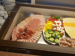 A buffet with various food items including sliced meats, cheeses, vegetables, and sausages.