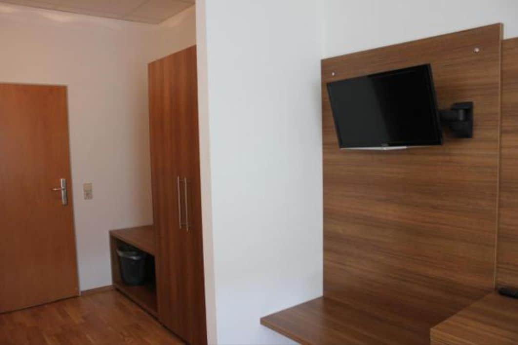 A modern room with a wooden wardrobe, a small trash bin, and a mounted television.