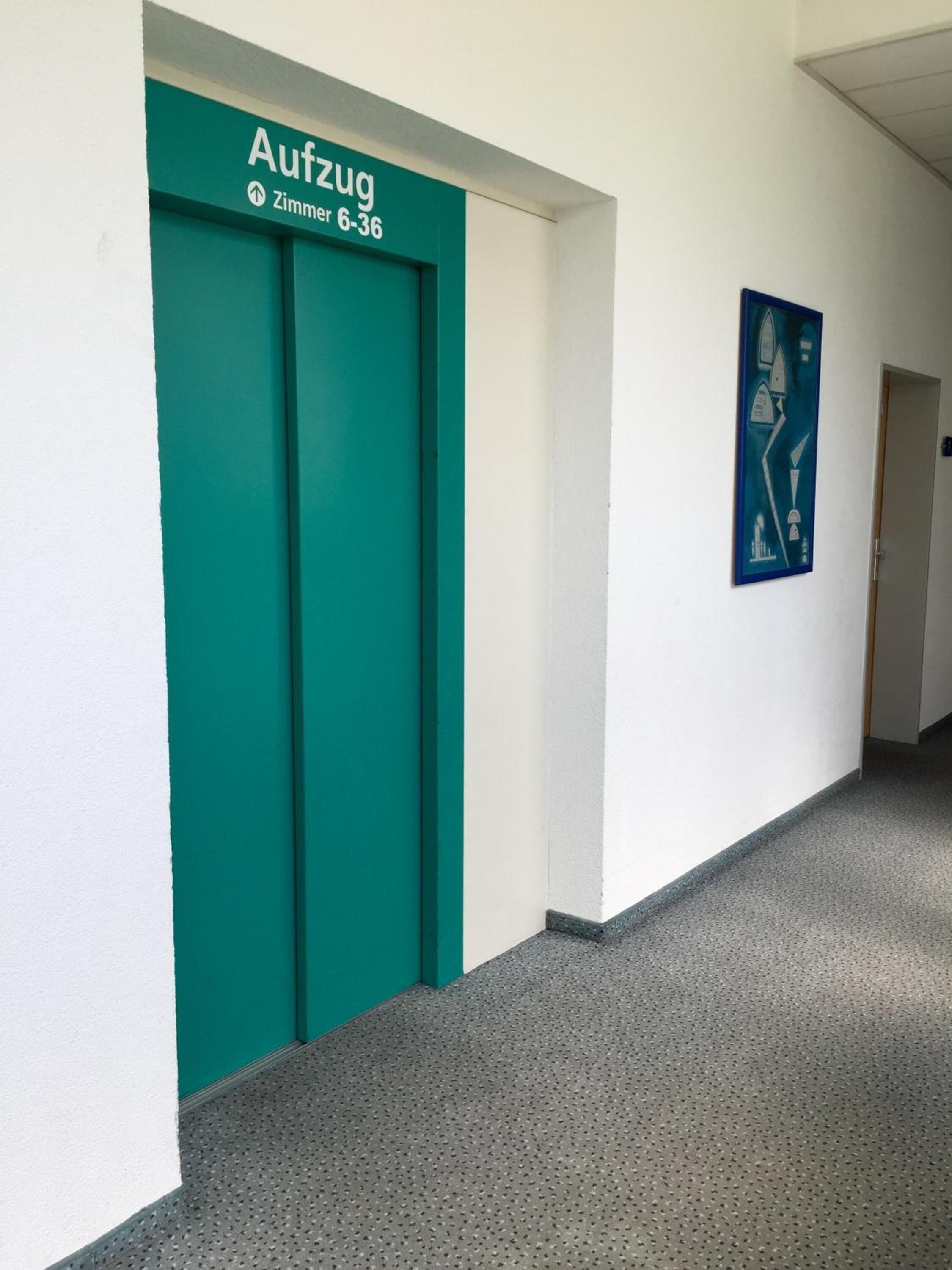 A hallway with a teal elevator marked "Aufzug Zimmer 6-36" and a blue abstract painting on the wall.