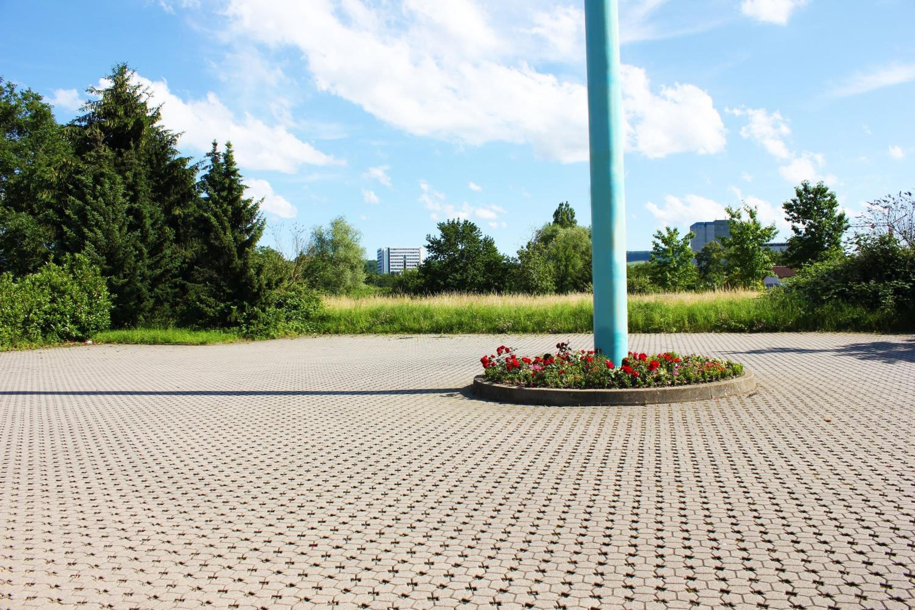 A paved plaza with a circular flower bed and a blue pole.