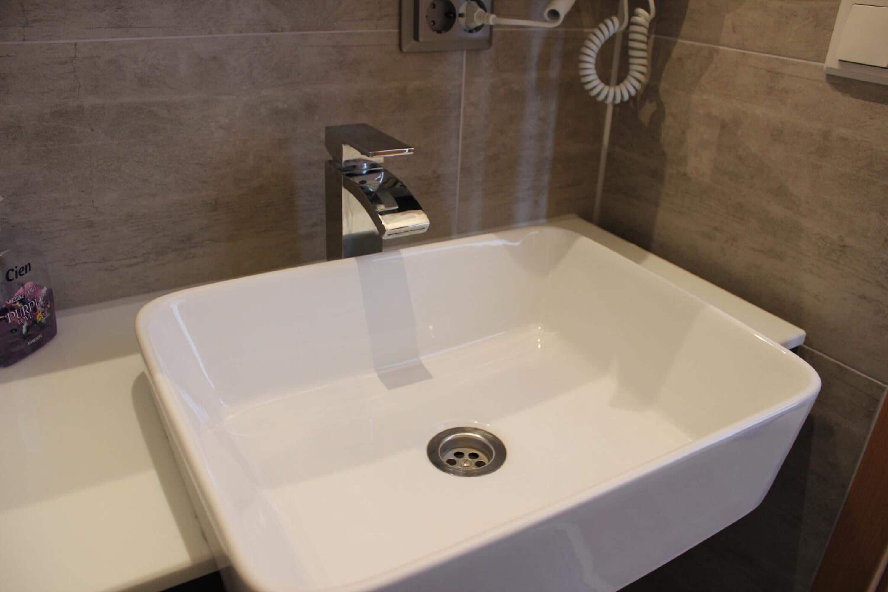 A white bathroom sink with a modern faucet and a wall-mounted towel dispenser.