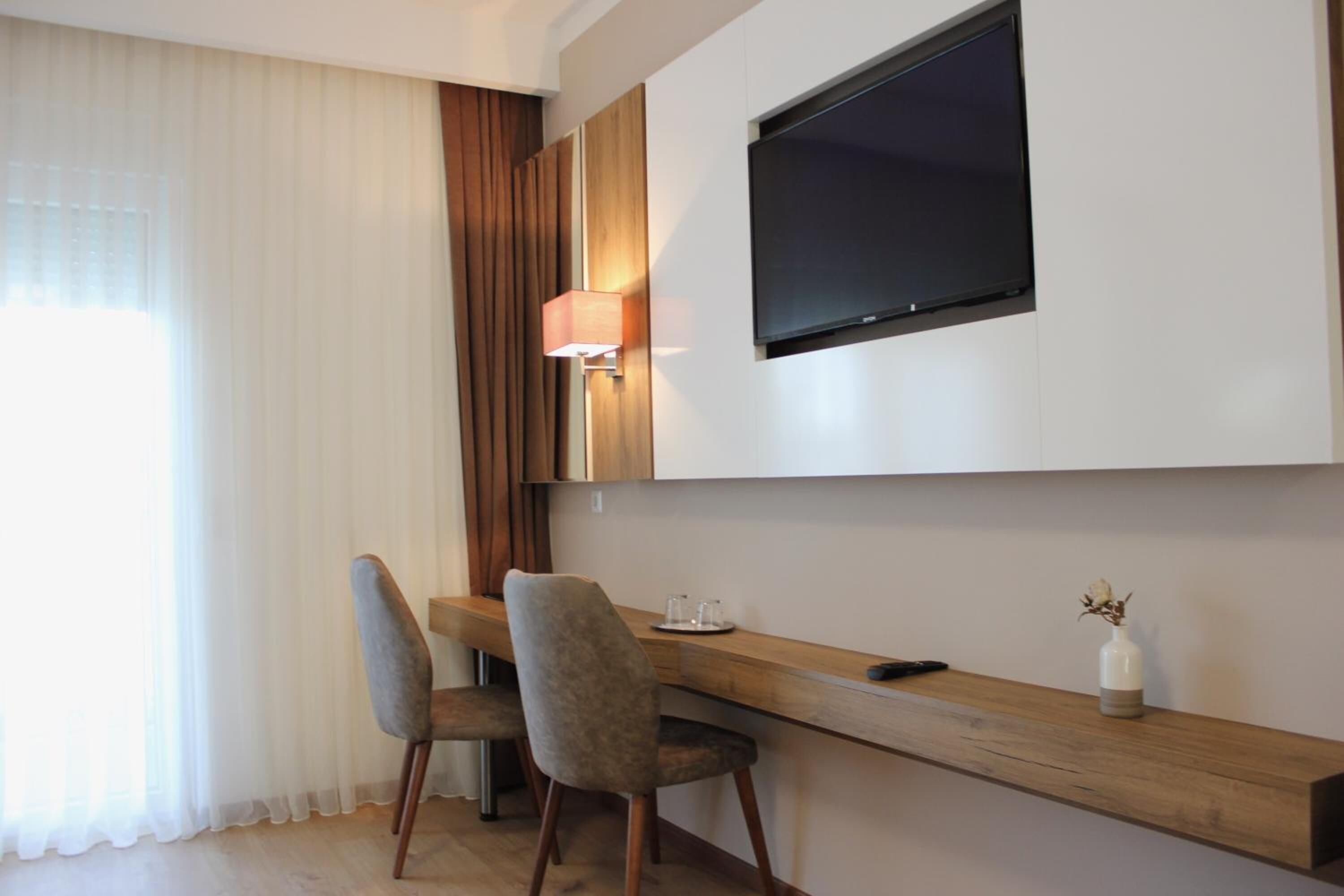 Una habitación moderna con un escritorio de madera, dos sillas, un televisor montado en la pared y una lámpara.