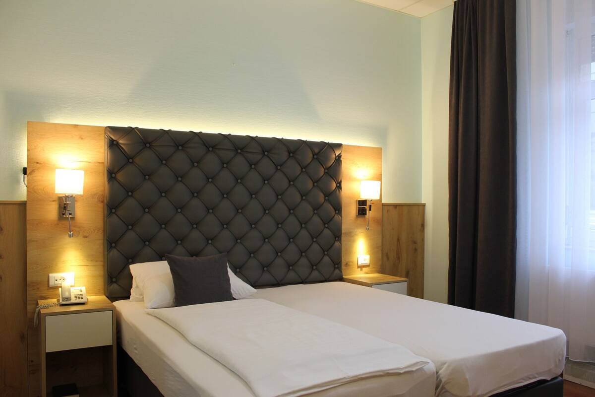A double bed with a tufted headboard, bedside lamps, and a wooden nightstand with a phone.