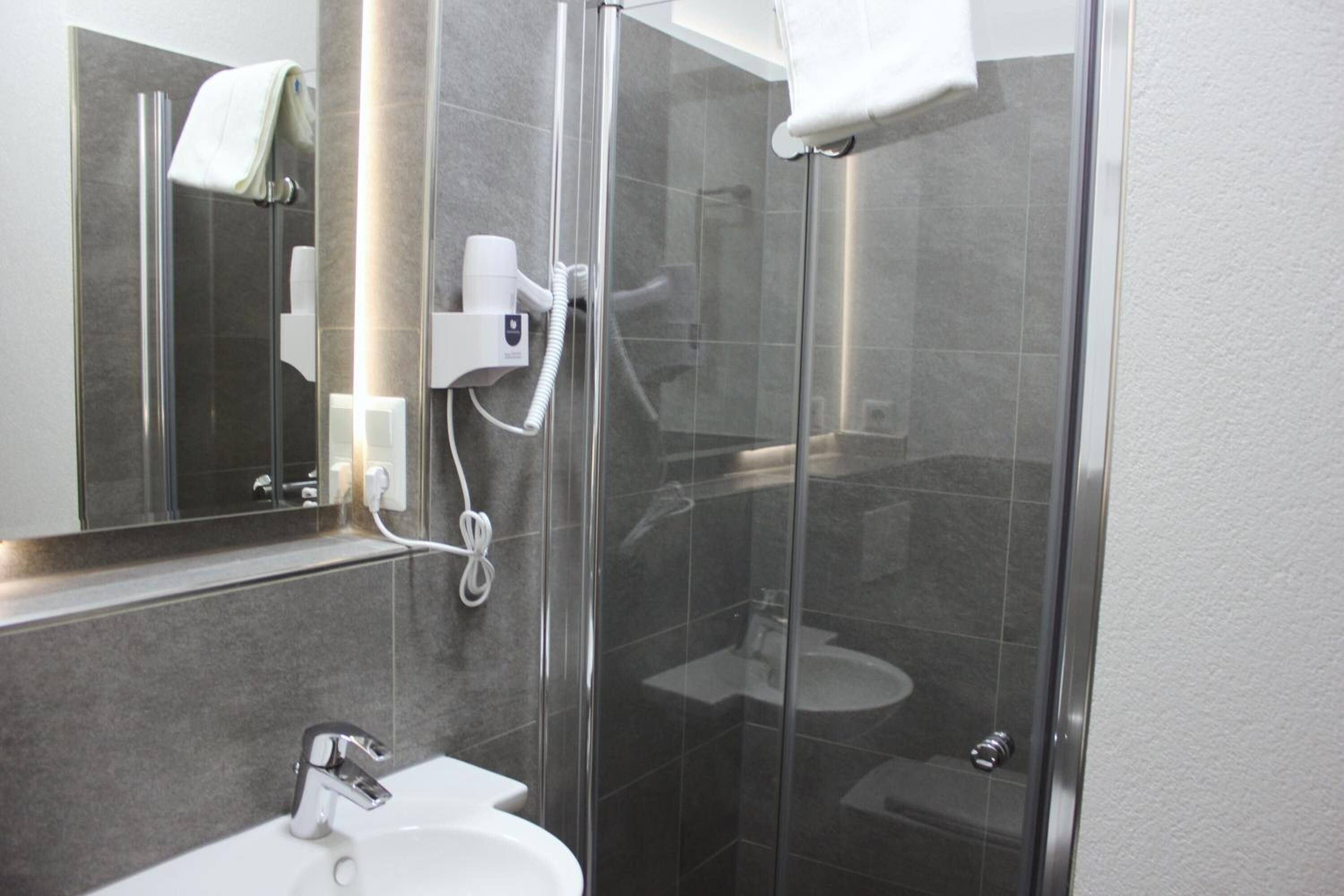 Une salle de bain moderne avec une douche à parois de verre, un lavabo blanc et un miroir au-dessus du lavabo.