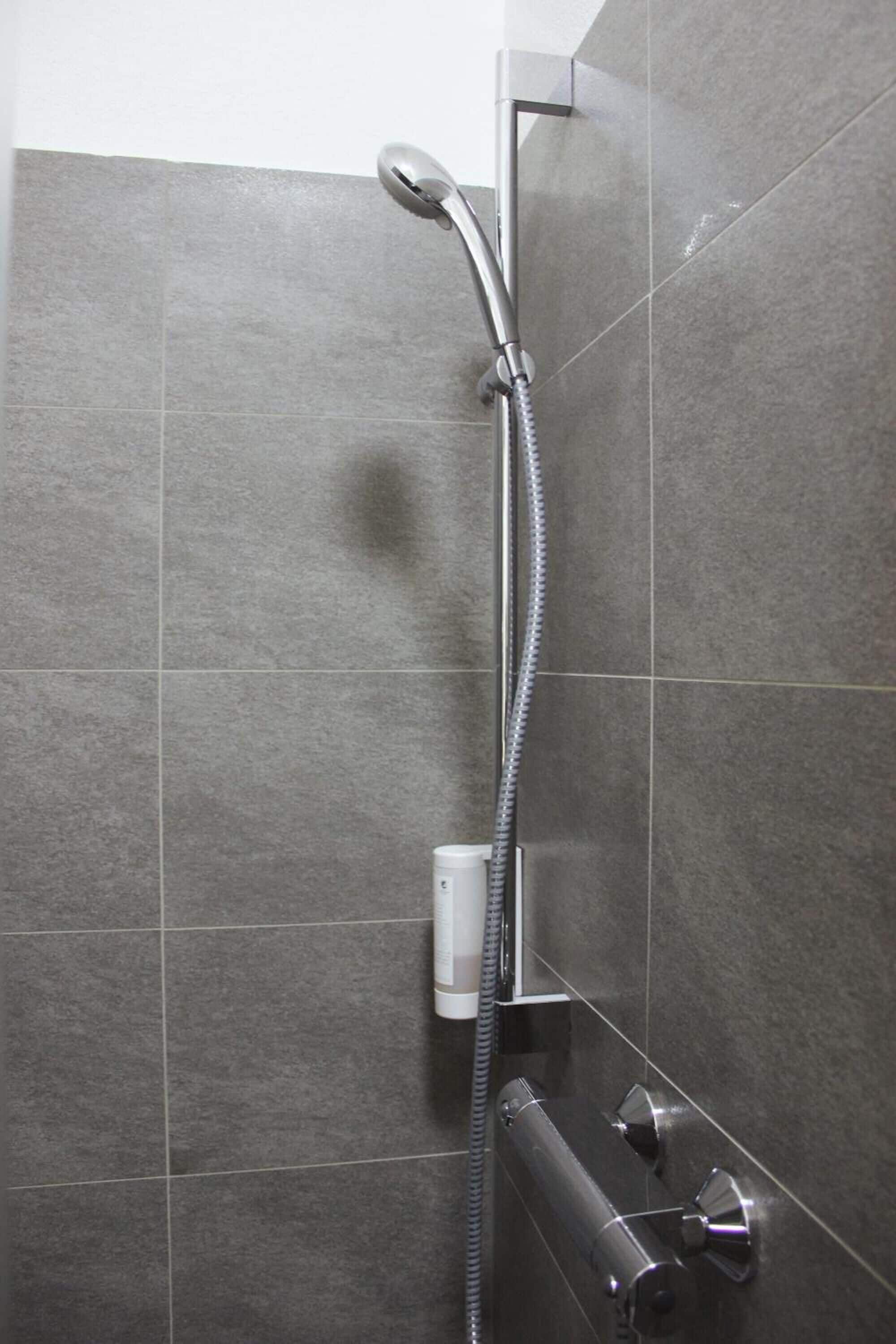 A shower with a handheld showerhead and a wall-mounted control panel.