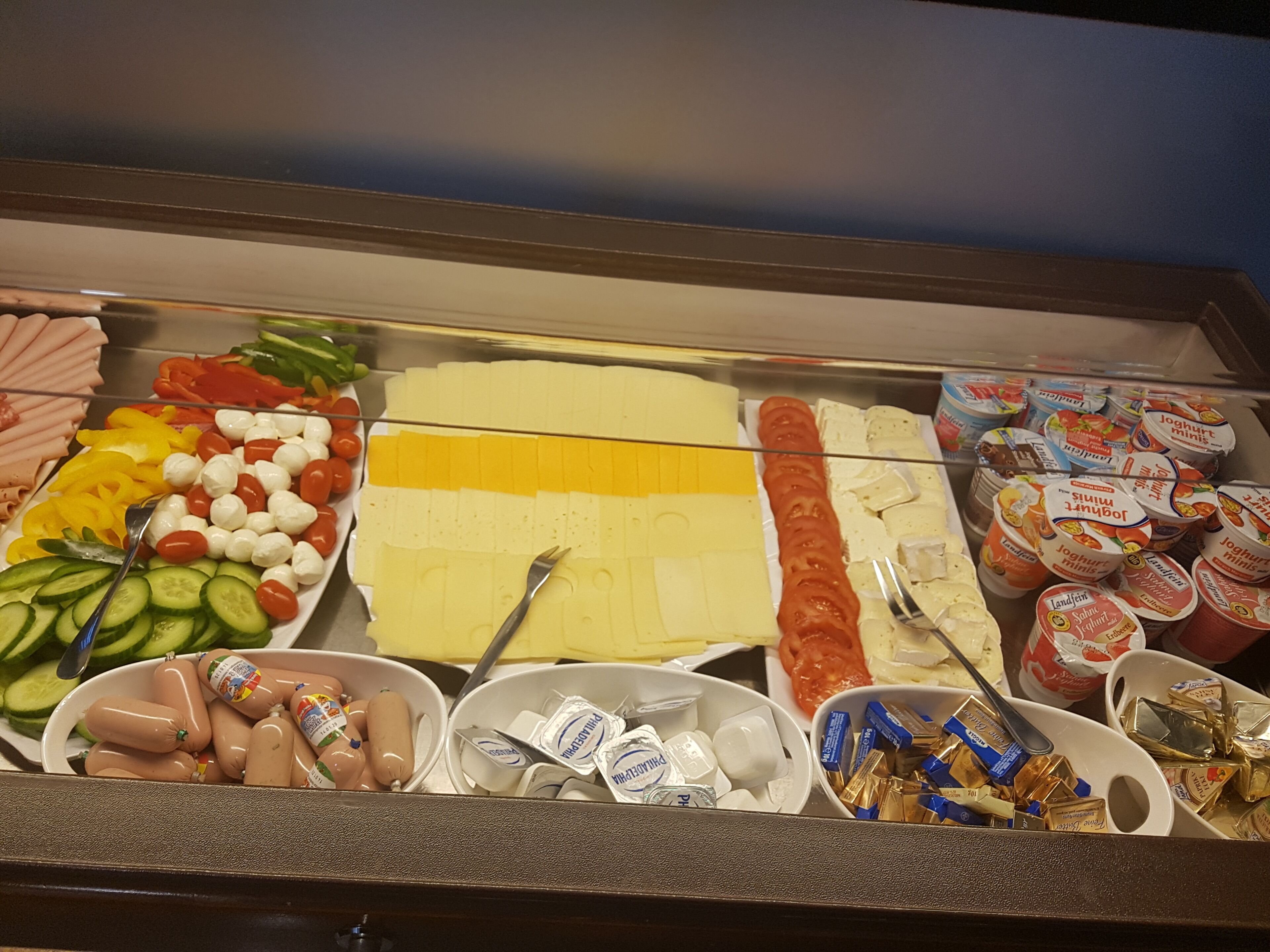 Un bufé con diversas opciones de comida, incluyendo carnes en rodajas, quesos, verduras y productos lácteos.