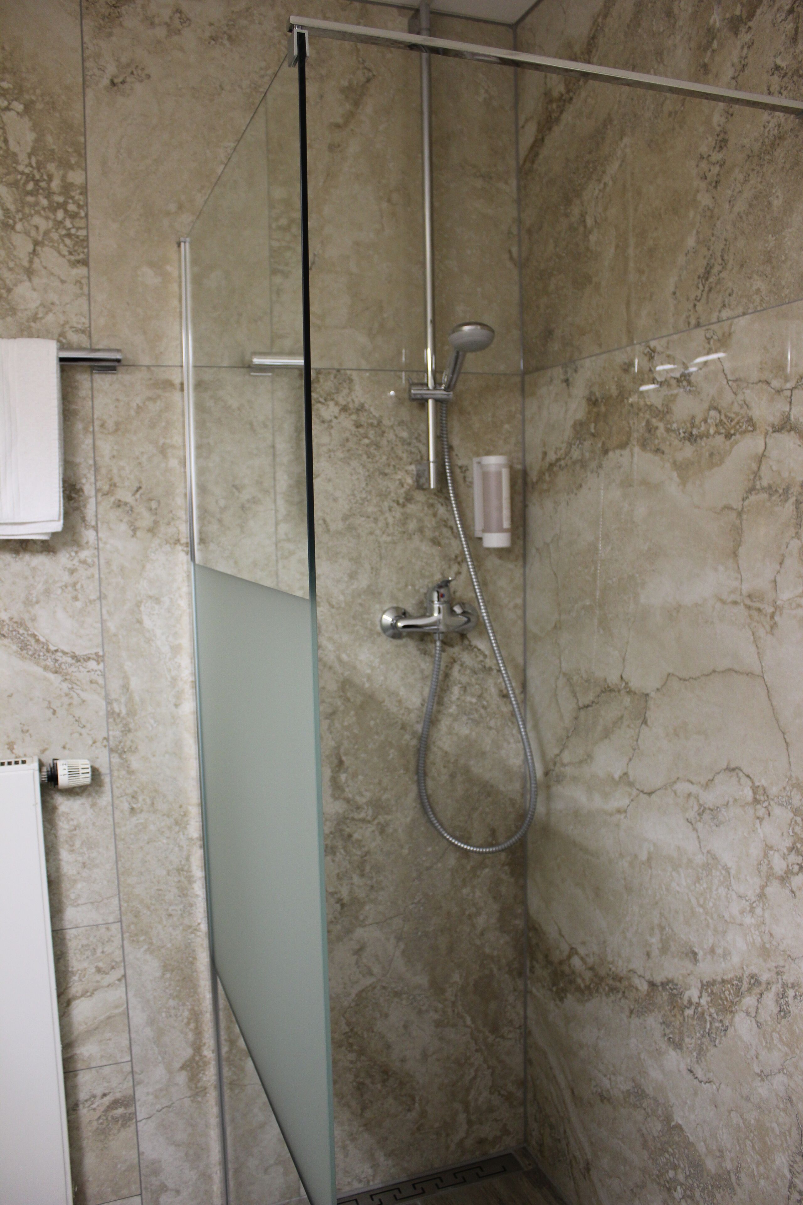 Une douche fermée par des parois en verre, dotée d’un pommeau de douche à main et d’un robinet mural.