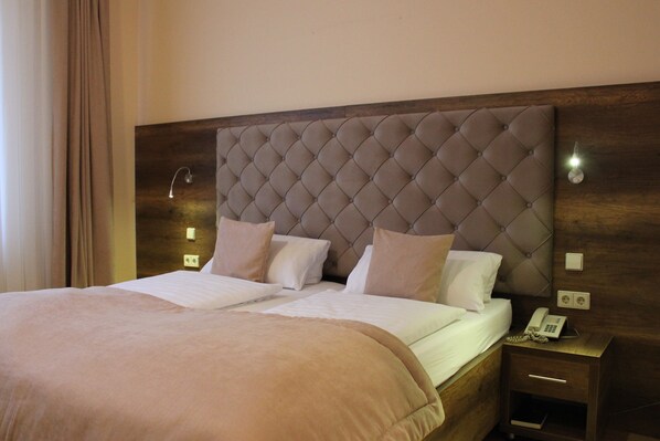 A double bed with a tufted headboard, two bedside tables with lamps, and a telephone on the right side.