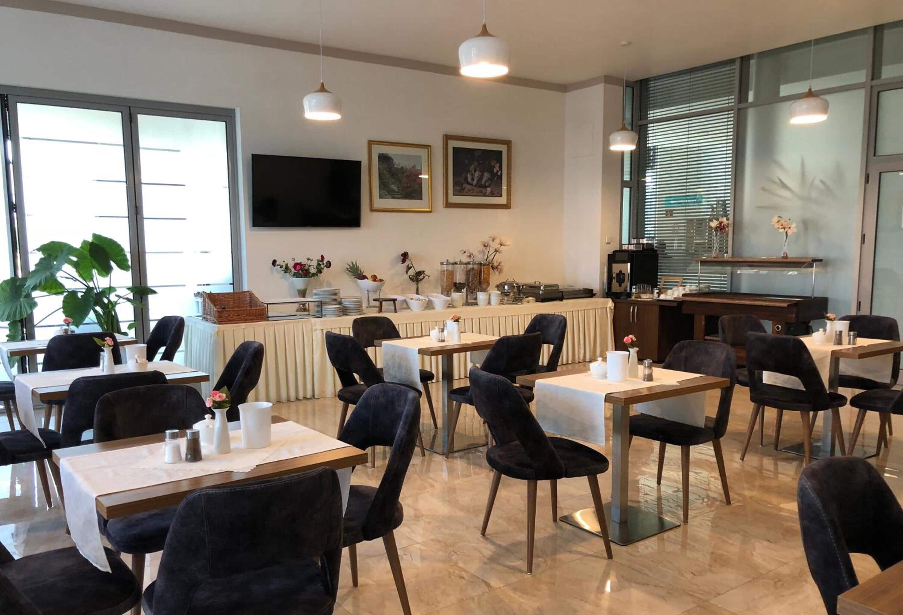 A dining area with tables and chairs, a counter with a cash register, and framed artwork on the wall.